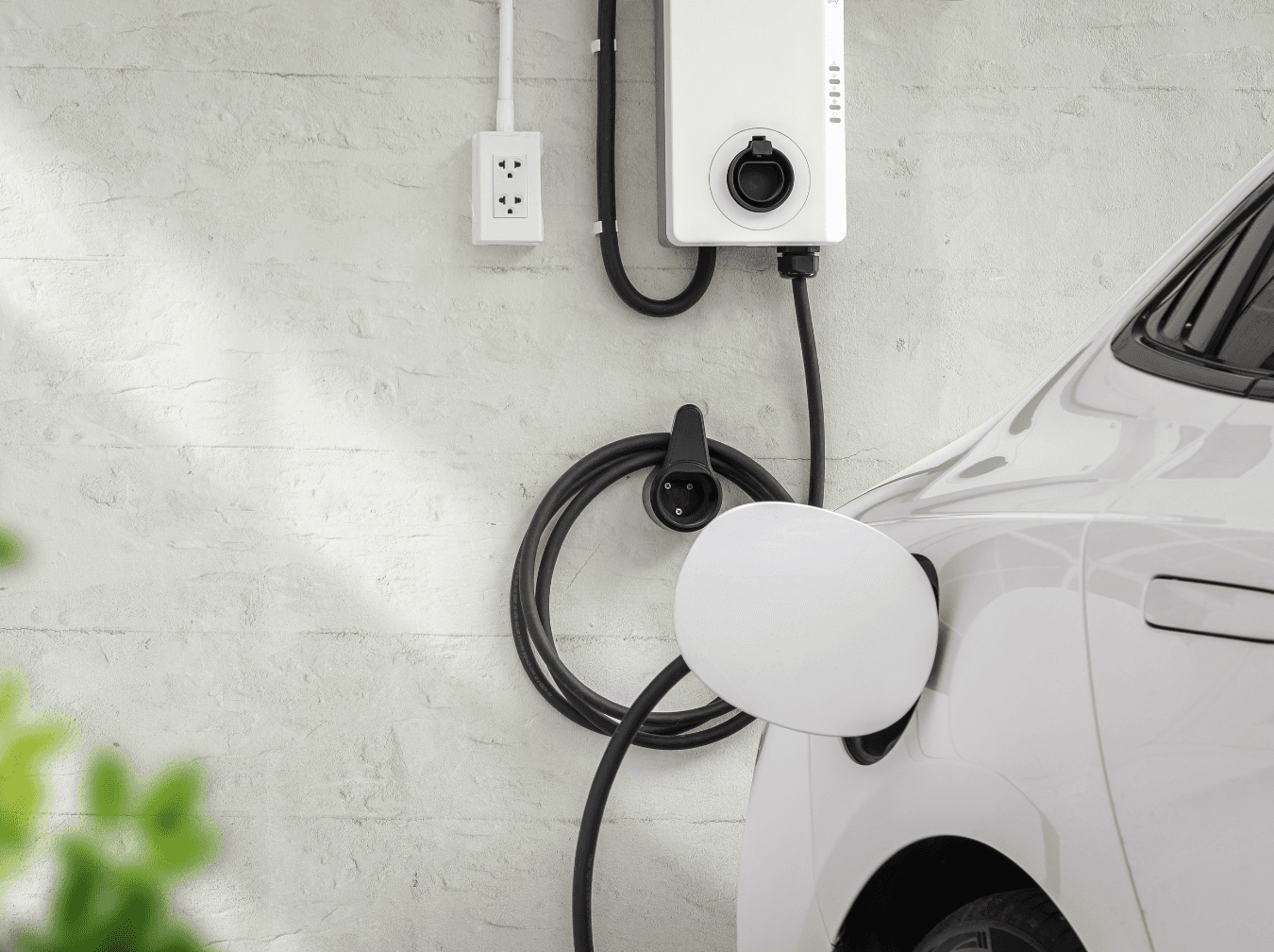 A white electric vehicle charging at a modern, wall-mounted EV charging station installed on a white brick wall.